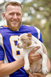 © Georgii - American football player with a dog posing on camera in a park. Copy space, sports banner. Concept american football, sport for the protection of animals.
