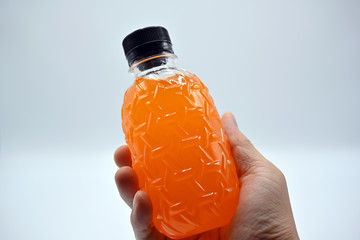 Wall Mural - The man's hand is holding a PET (Polyethylene Terephthalate) plastic bottle, a black lid with fresh orange juice on a white background.