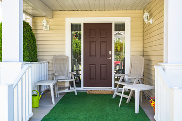 Family house main entrance with blossoming flowers and chairs under the porch