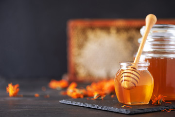 Wall Mural - Herbal honey in jar with dipper, honeycomb, bee pollen granules, calendula flowers on black background.