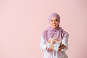 Wall Mural - Beautiful mature Muslim woman with gift box on color background