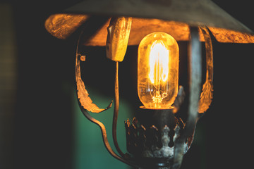 Old and dusty lamp with a long bulb shines with a orange, warm light in the dark room.