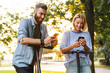 © Drobot Dean - Image of cute smiling couple typing on cellphones while riding e-scooters