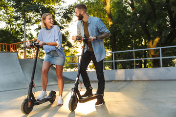 Sticker - Image of young happy couple smiling while riding e-scooters