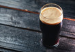 A glass of dark craft beer porter on a wooden table in a pub with copyspace