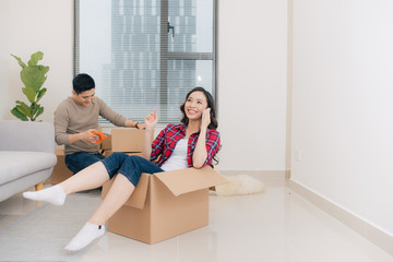 Wall Mural - Happy young couple moving in their new apartment, having fun and riding in cardboard boxes at new home