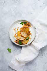 Wall Mural - Greek yogurt with caramelized pear, granola, nuts and melted sugar for a wholesome breakfast on a gray ceramic plate. Rustic style. Top view.