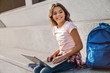 Side view shot of preteen schoolgirl sitting on the stairs with backpack outside and using laptop