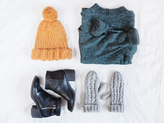 Wall Mural - Woman's winter outfit accessories with green woolen sweater, black ankle boots, knitted mustard hat and grey gloves. Flat lay. Top view