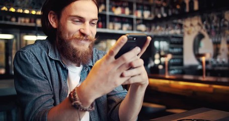 Stylish young male in casual outfit with bracelet on wrist chatting on smartphone, spending time in cafe, modern life