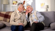 © motortion - Old man talking to deaf friend sitting on sofa at home, hearing disease, problem