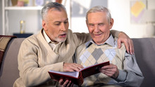 Happy Senior Brothers Watching Family Album On Home Sofa, Pleasant Memories