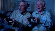 © motortion - Excited retired men playing video game at night together, friendship connection