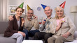 © motortion - Smiling aged group of people in party hats looking camera holding noisemakers