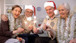 © motortion - Men in Santa Claus hats and women wrapped in tinsels holding sparklers, New Year