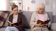 © motortion - Two offended old women reading books sitting nursing home sofa, misunderstanding