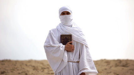 Wall Mural - Arab pilgrim holding Koran in desert, preacher of Islamic faith and teachings