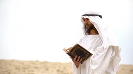 Wall Mural - Arab reading Koran in desert, meditating and reflecting on Muhammad teachings