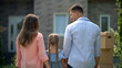 © motortion - Family moving in, looking at each other in front of new house, back view