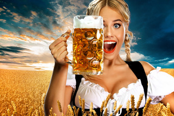 Smiling young sexy oktoberfest girl waitress, wearing a traditional Bavarian or german dirndl, serving big beer mug with drink outdoor.