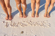High angle view of four female legs barefoot feet standing on the sand beach by the Thassos written on the sand