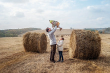 A Boy And A Girl Near A Haystack In A Field At Sun Day On Autumn Next To A Tractor Cleans Field