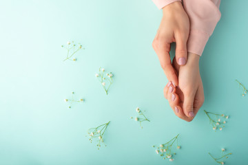 Wall Mural - Flat lay. Tender female hands with white delicate flowers. On a turquoise background. Art photo, top view, horizontal photo.