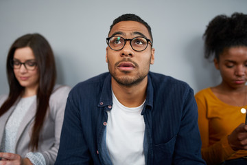 Wall Mural - Worried young african american man expecting his turn for interview sitting with other female candidates