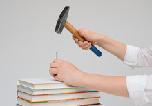 Children's Hands Hammer A Nail Into A Pile Of Books