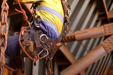 Closeup picture of male rope access inspector worker wearing full safety harness setting on a chair, abseiling performing wall leaking inspection working at height construction site, Sydney, Australia