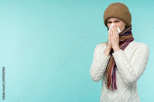 Cuadros en Lienzo Health and medicine concept - Young woman blowing nose into tissue, on a blue background
