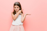 Little girl wearing a princess look excited holding a copy space on palm.