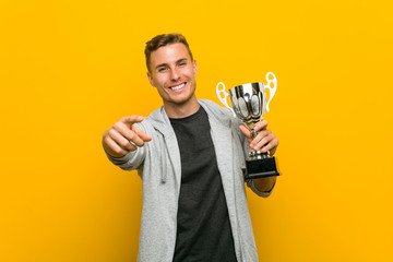 young caucasian man holding a trophy cheerful smiles pointing to front.