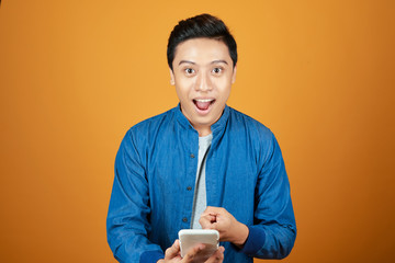 Wall Mural - Young asian man surprised when he looking smartphone. On orange background