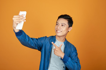 Wall Mural - Young happy Asian man selfie with smartphone in colorful orange background