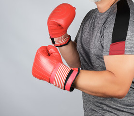 muscular adult athlete in gray uniform and red leather boxing gloves