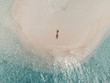 Aerial view of a sandbank in the Maldives sea - A young woman is lying on the white sand looking in the air with hands up