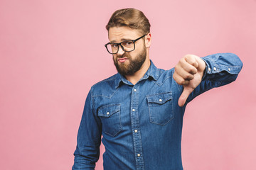 Stylish fashionable male poses indoors against pink background, assess project, shows sign of dislike, looks with negative expression and disapproval. Disagreement, disgust and negative expressions