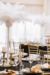 Stylish chairs and elegant gold-plated details. Black tablecloths on big, round tables for a wedding lunch.