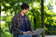 © ianachyrva - Young bearded brunet student with mustache sitting with a laptop in a park. Distance learning