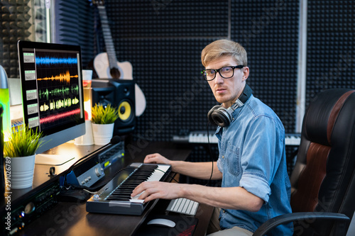 Fotografía Young man with headphones looking at you while sitting in recording studio