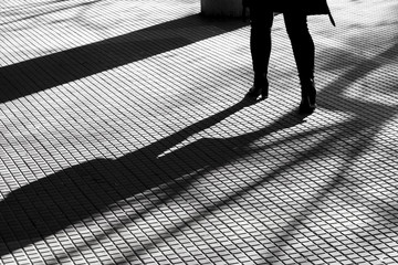 Wall Mural - Blurry silhouette shadow of legs of a woman in high heels walking alone on tiled pedestrian walkway