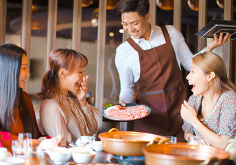 Happy waiter  bring  beef slices  and serving group of friends in restaurant.