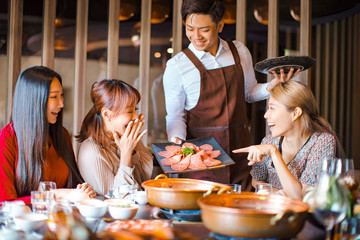 Wall Mural - Happy waiter  bring  beef slices  and serving group of friends in restaurant.