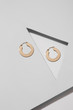 Closeup shot of congo earrings made of shiny golden metal in the shape of wide flat ring. The pair of earrings is isolated on the gray background with geometryc details. 