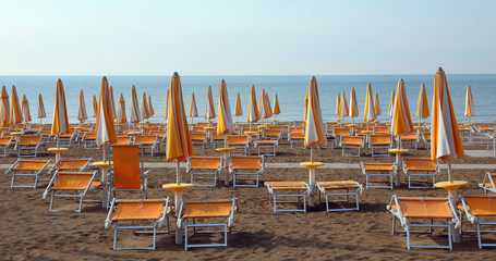 Wall Mural - closed umbrellas with deckchairs on the beach without people in