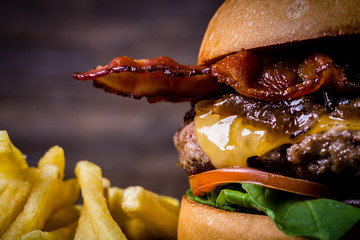 Craft beef burger with cheese, bacon, rocket leafs, caramelize onion and french fries on wood table and rustic background.