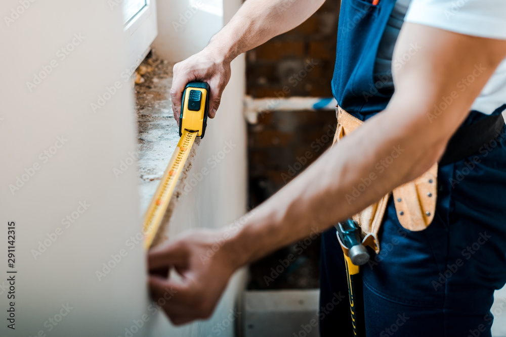 cropped view of handyman measuring wall with yellow measuring tape - obrazy, fototapety, plakaty 