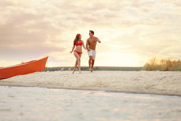 Poster - Happy young couple running together on sea beach at sunset