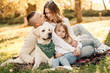 © zadorozhna - Happy beautiful family with dog labrador is having fun  are sitting on green grass in park.